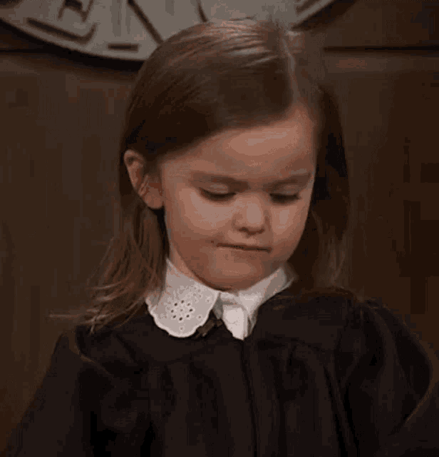 a little girl in a black dress and white collar is making a face .