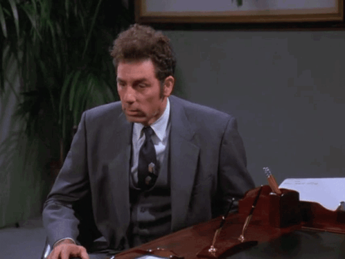 a man in a suit and tie sits at a desk with the words  i don 't even really work here  above him