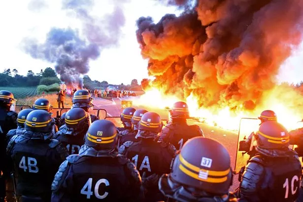 Riot-police-stand-guard-behind-a-fire-as-refinery-workers-hold-a-blockade-of-the-oil-depot-of-Douchy-Les-Mines.jpg